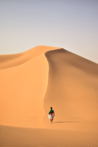 Un voyageur solitaire marchant sur les vastes dunes de sable doré du désert du Sahara en Algérie.