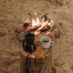 Un cadre serein autour d'un feu de camp avec café et cafetière moka sur une bûche de bois, parfait pour les amoureux du plein air.