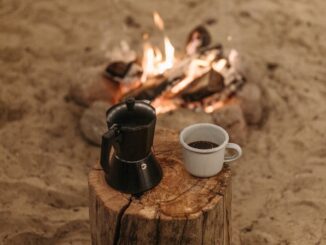 Un cadre serein autour d'un feu de camp avec café et cafetière moka sur une bûche de bois, parfait pour les amoureux du plein air.