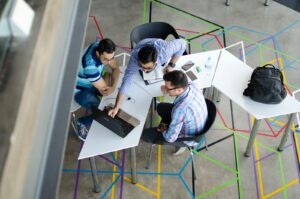 Trois hommes collaborant sur un ordinateur portable dans un espace de bureau moderne au thème géométrique.